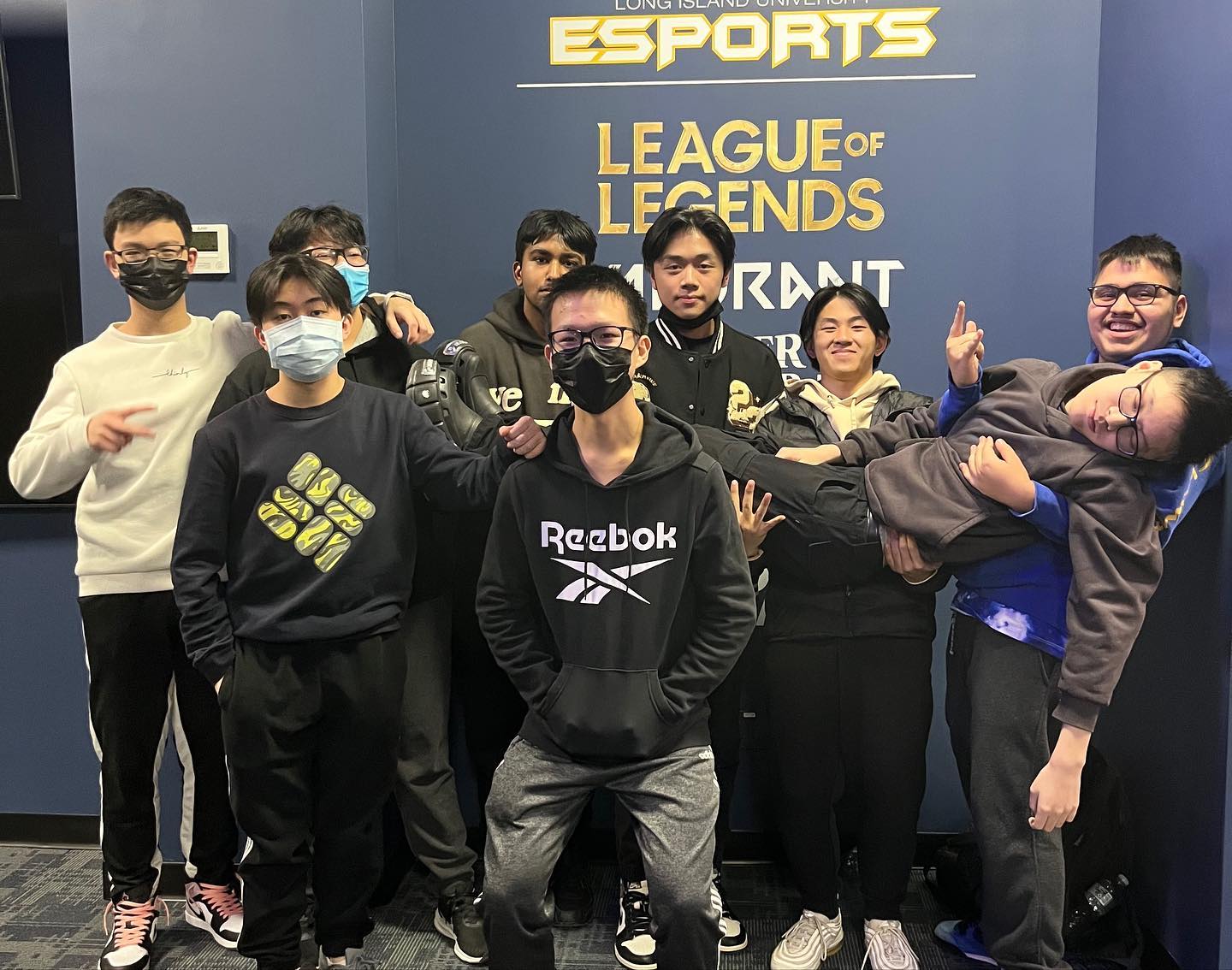 Group photo at the banner, one teammate being playfully carried