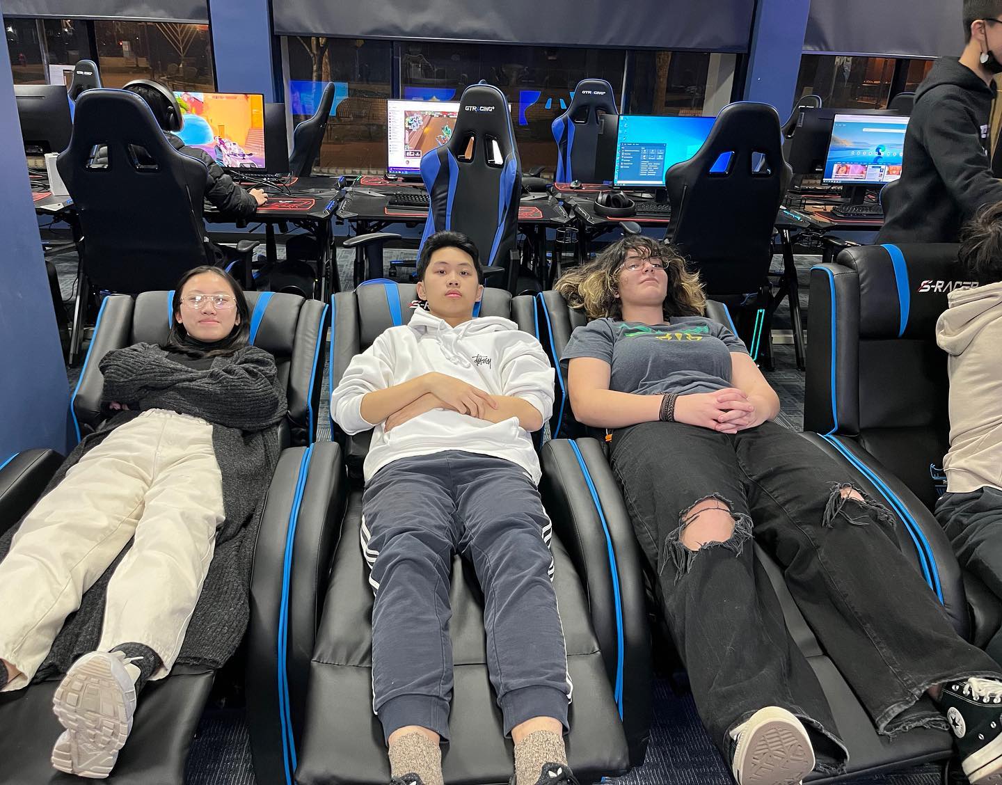 Three students lounging back in the gaming chairs