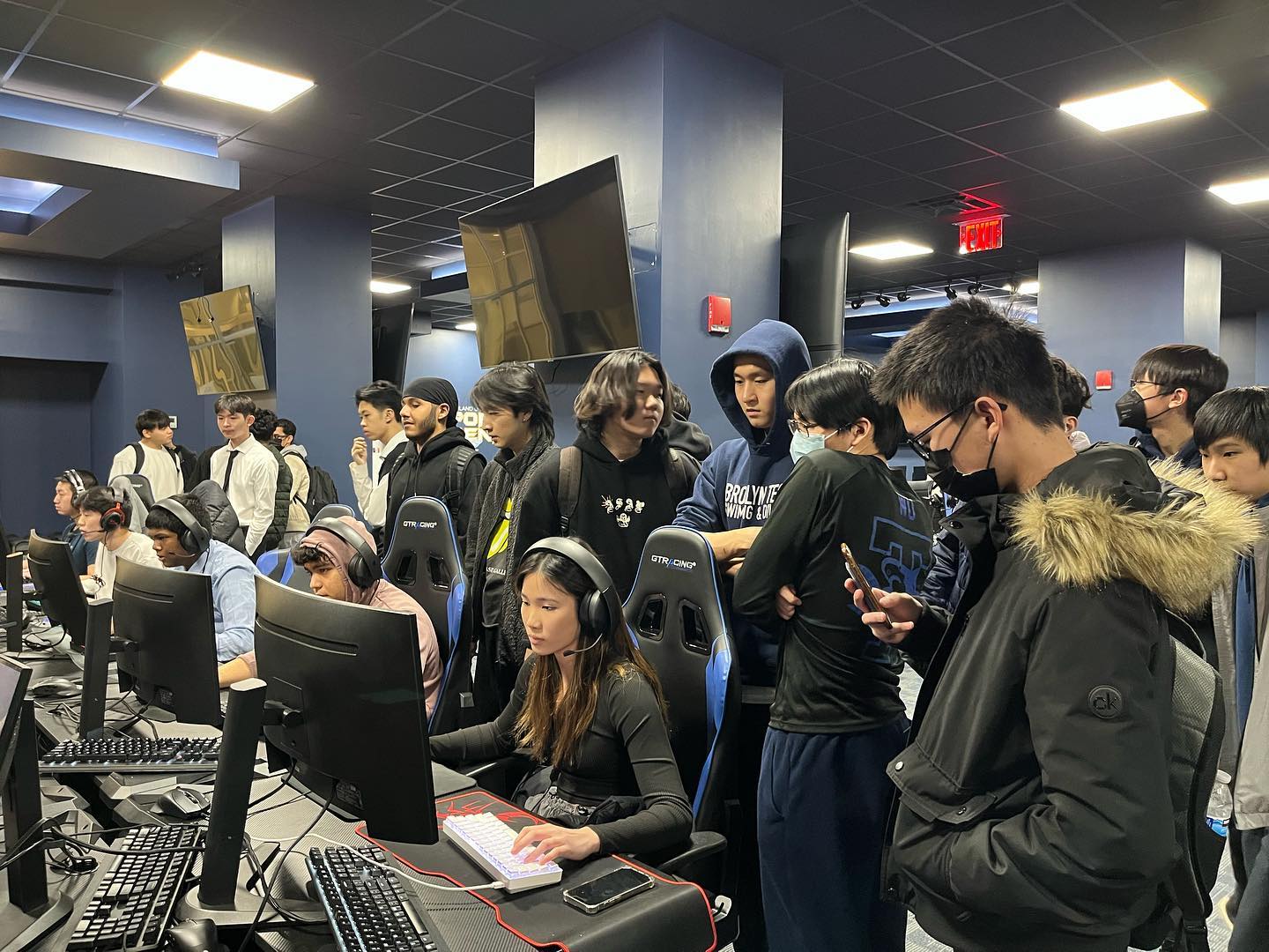 Crowd of students gathered around the gaming stations watching a match live